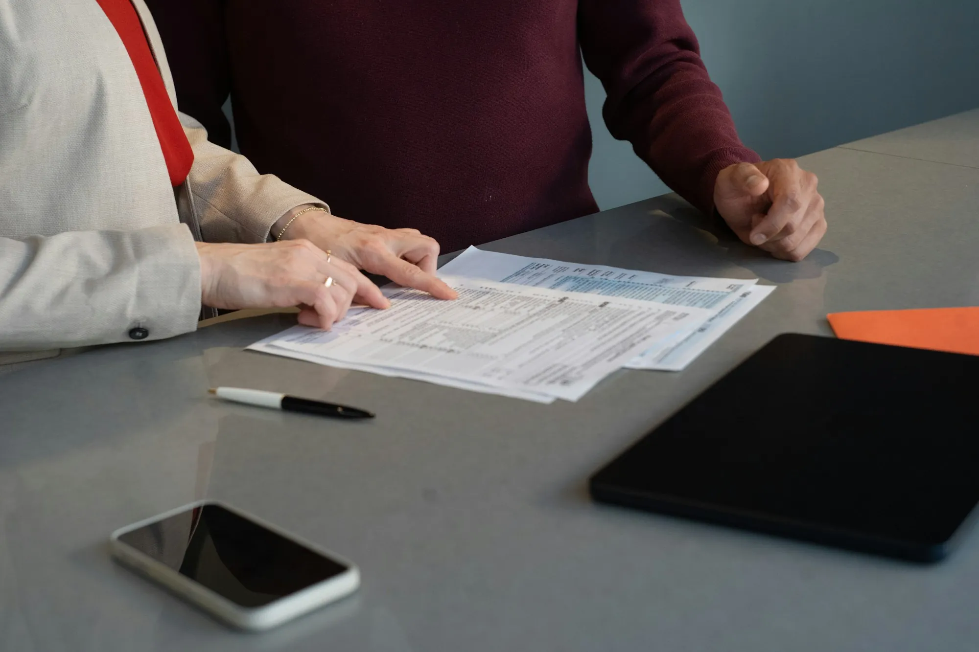 People reviewing printed forms beside a tablet and phone