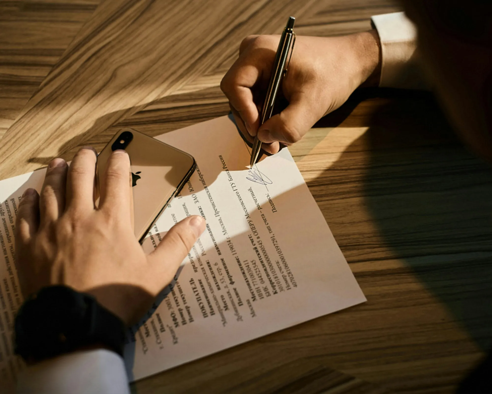 Hands filling out paperwork on a wooden desk
